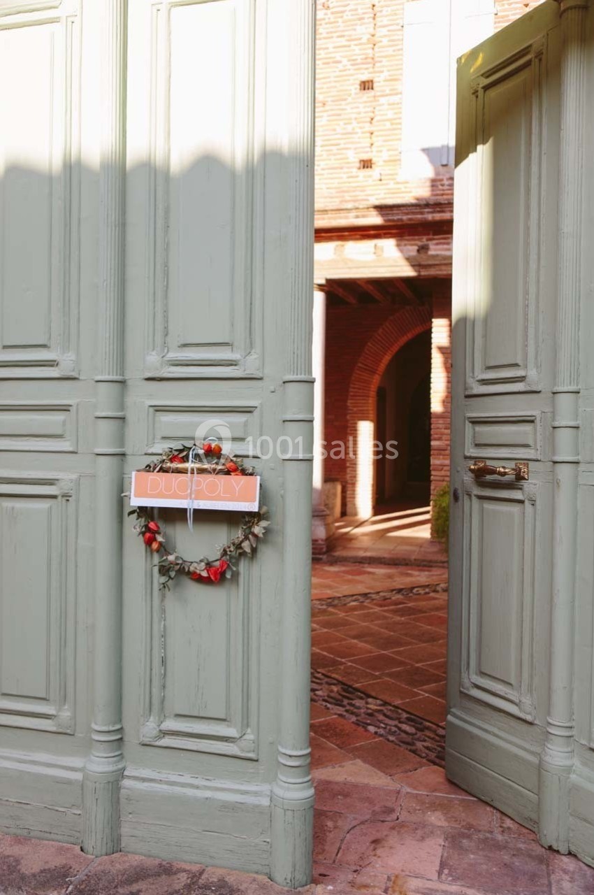 Porte verte entrouverte avec une cour pavée en arrière-plan, décorée d'une couronne ornée de baies rouges.