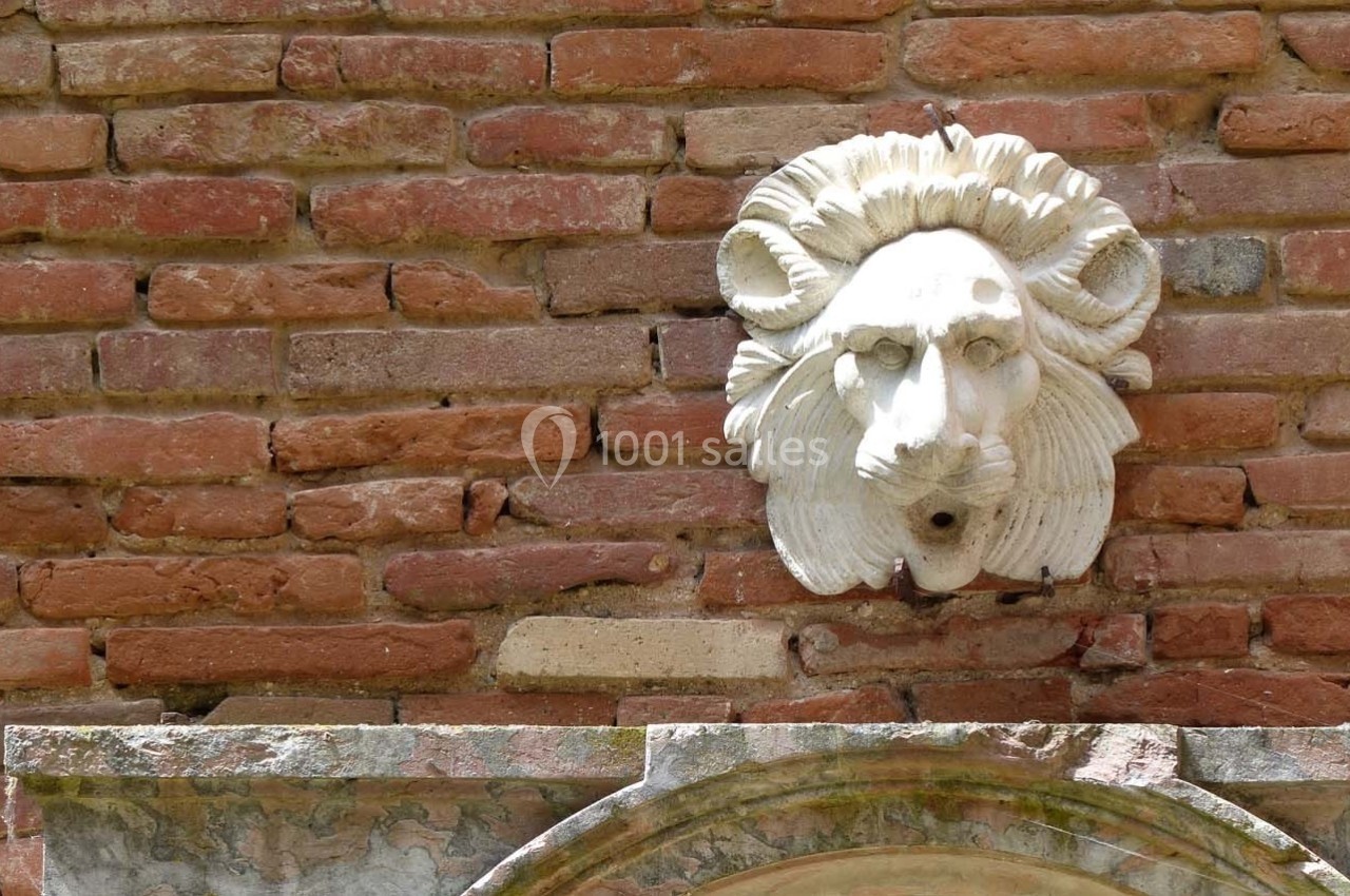 Bas-relief en pierre représentant une tête de lion sculptée, fixé sur un mur de briques rouges.
