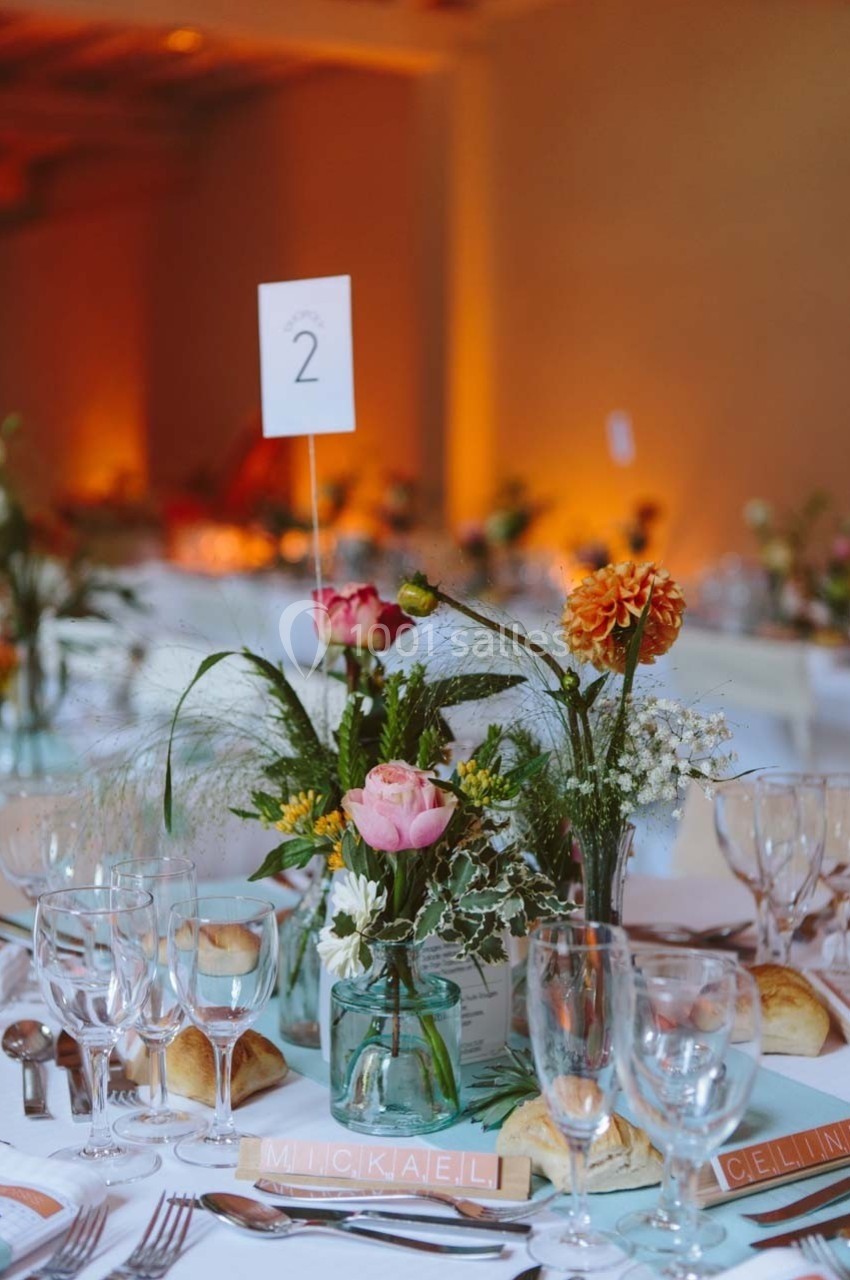 Table de réception décorée avec des fleurs colorées, des verres, des assiettes et un marque-place avec un numéro.