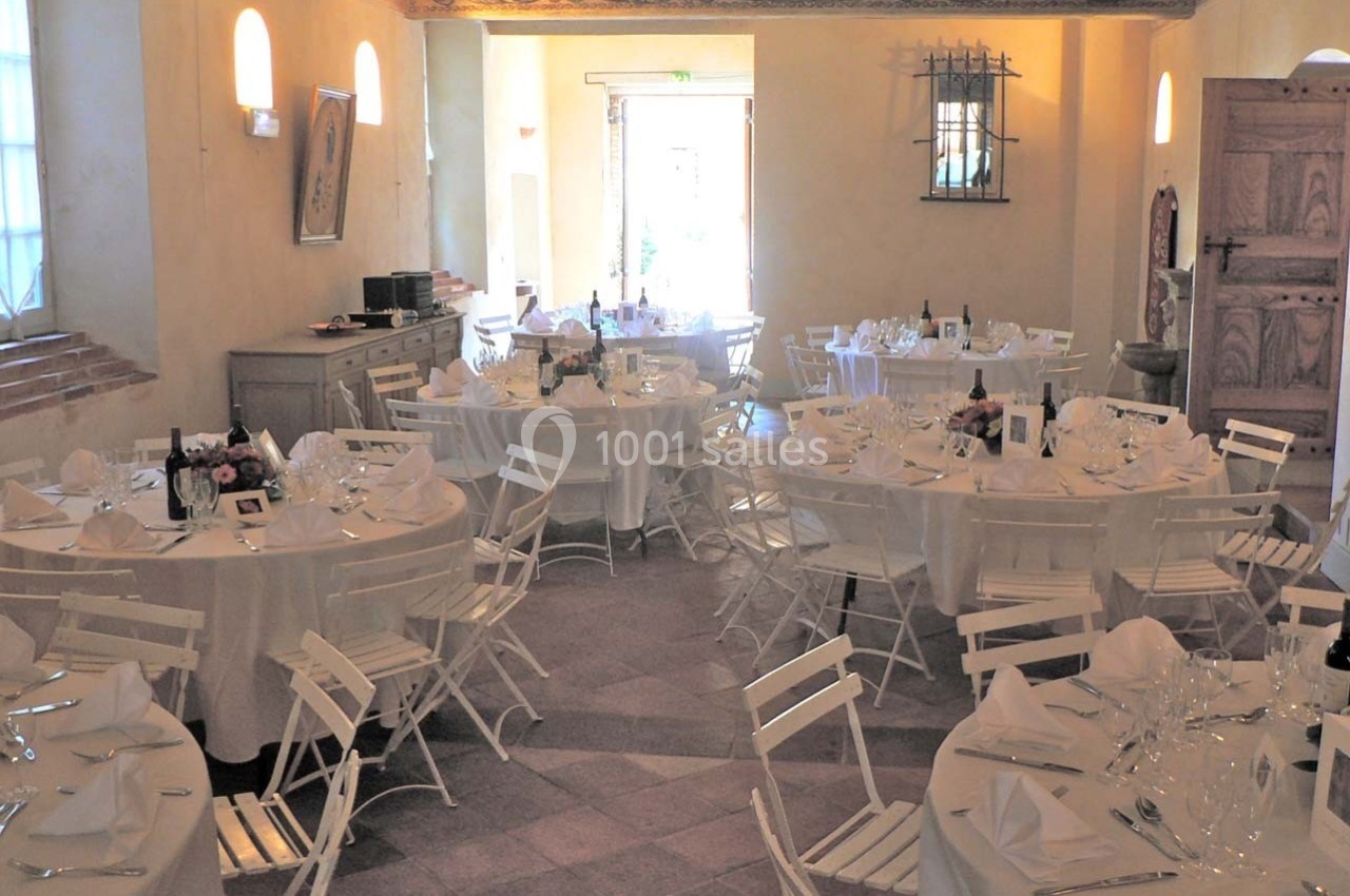 Salle de réception lumineuse avec des tables rondes dressées, nappes blanches et chaises pliantes blanches.