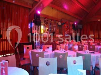 Salle décorée avec des tables rondes dressées, éclairage coloré et scène en fond avec des éléments rétro.