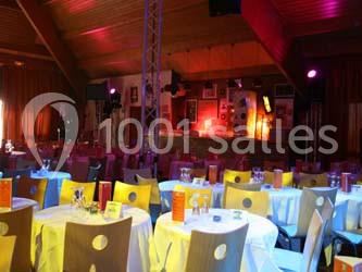 Salle de réception avec tables rondes dressées, chaises colorées et éclairage tamisé.