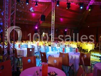Salle de réception illuminée par des lumières colorées, avec des tables rondes dressées et des chaises disposées autour.