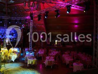 Salle de réception avec tables dressées, éclairage coloré et projecteurs suspendus au plafond.