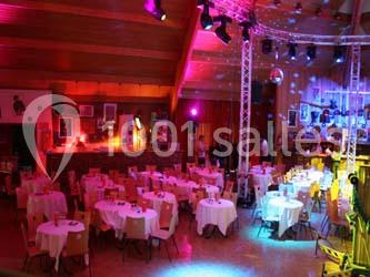 Salle décorée pour un événement, avec tables rondes dressées, éclairages colorés et ambiance festive.