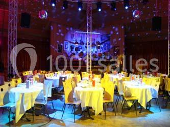 Salle de réception décorée avec des tables rondes dressées, éclairage coloré et ambiance festive.