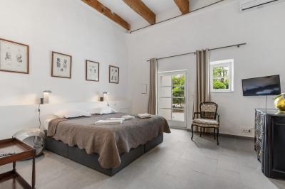 Miniature Location salle Servian (Hérault) - Château Hermitage de Combas #28 Chambre lumineuse avec lit double, tête de lit rouge, murs en pierre, grandes fenêtres et mobilier classique.