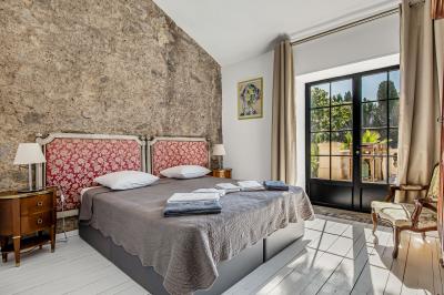 Miniature Location salle Servian (Hérault) - Château Hermitage de Combas #35 Chambre lumineuse avec lit double, tête de lit rouge, murs en pierre, grandes fenêtres et mobilier classique.