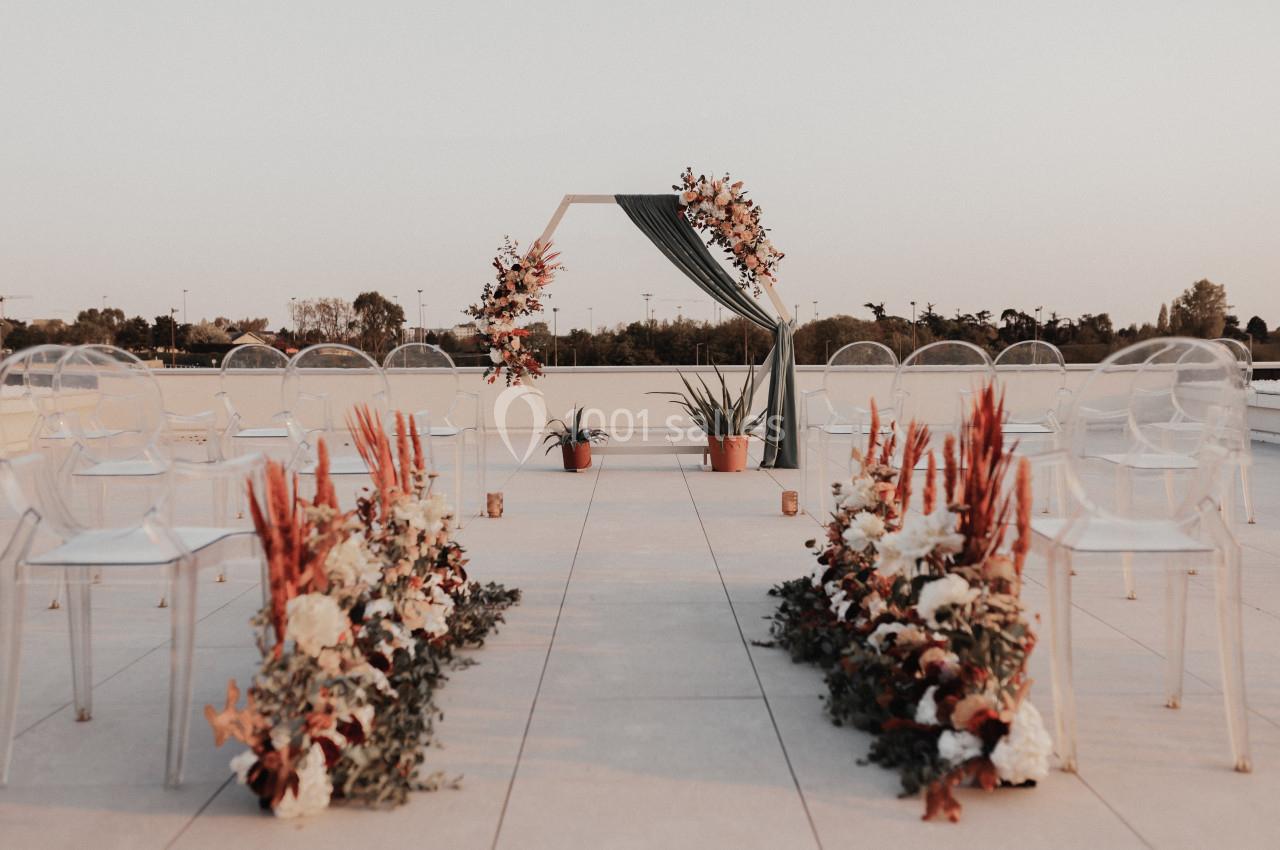 Rooftop Allée décorée de fleurs menant à une arche ornée de feuillages et fleurs, installée sur une terrasse extérieure.
