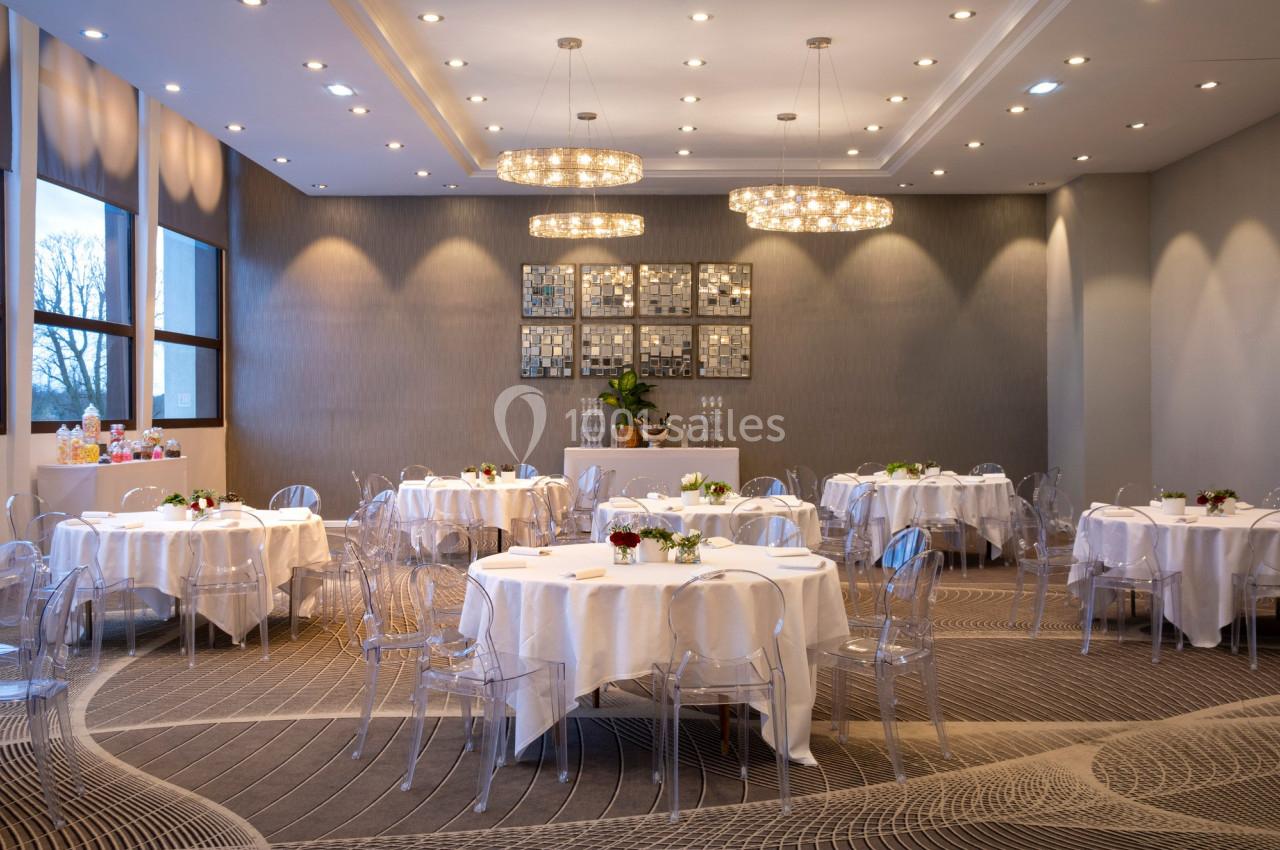 Salon Galerie Salle de réception lumineuse avec tables rondes dressées, chaises transparentes et décorations modernes.