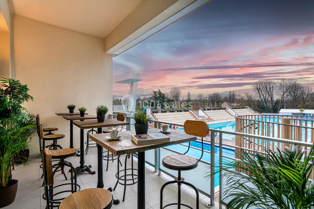 Terrasse Terrasse aménagée avec tables et plantes, offrant une vue sur une piscine extérieure et un ciel au coucher du soleil.