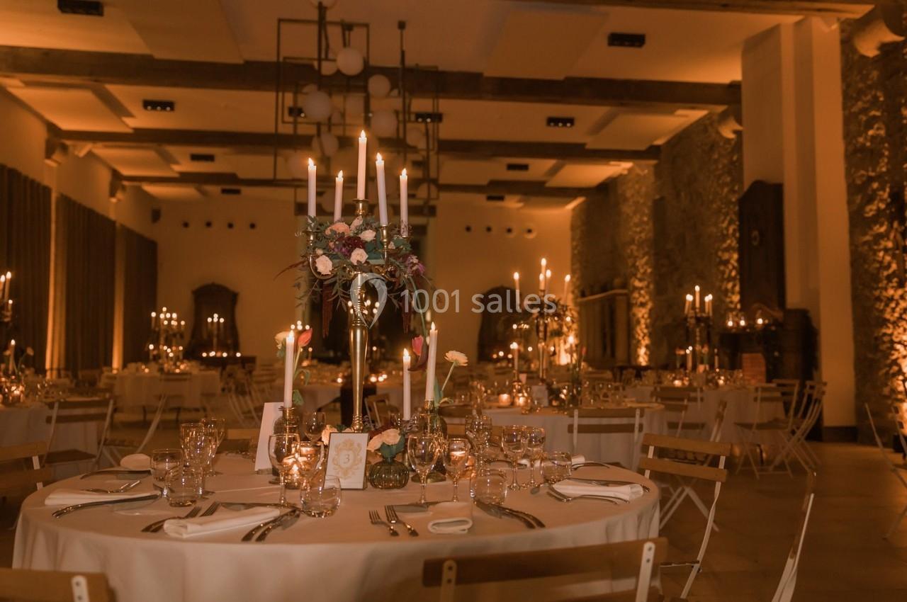 Salle de réception élégamment décorée avec des tables rondes, chandeliers et éclairage tamisé.