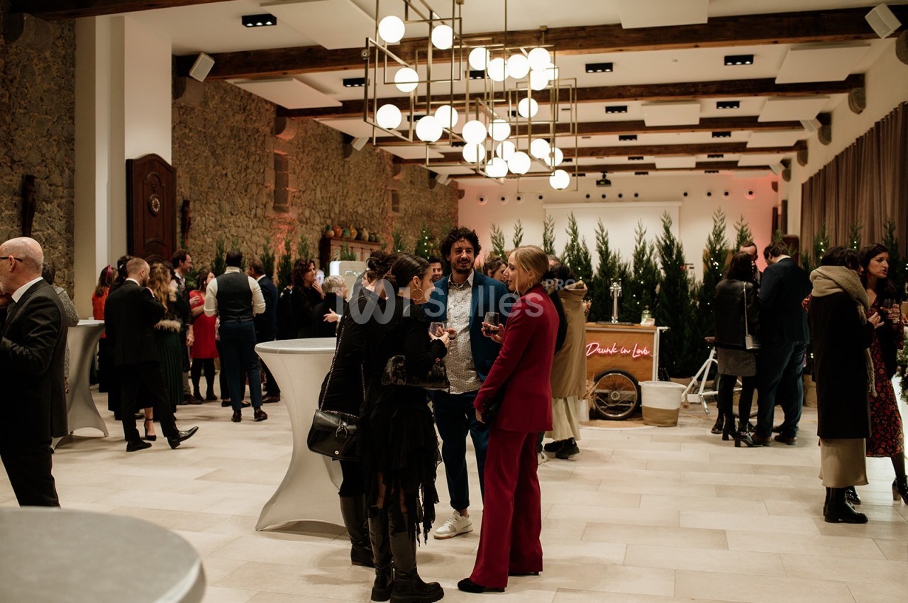 Personnes discutant dans une salle élégante avec des tables hautes, des luminaires modernes et une décoration festive.