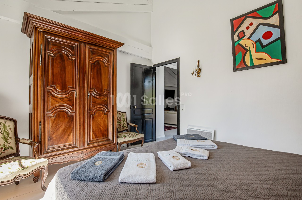 Chambre avec armoire en bois, lit recouvert d'une couverture marron et serviettes pliées, décorée d'un tableau coloré.