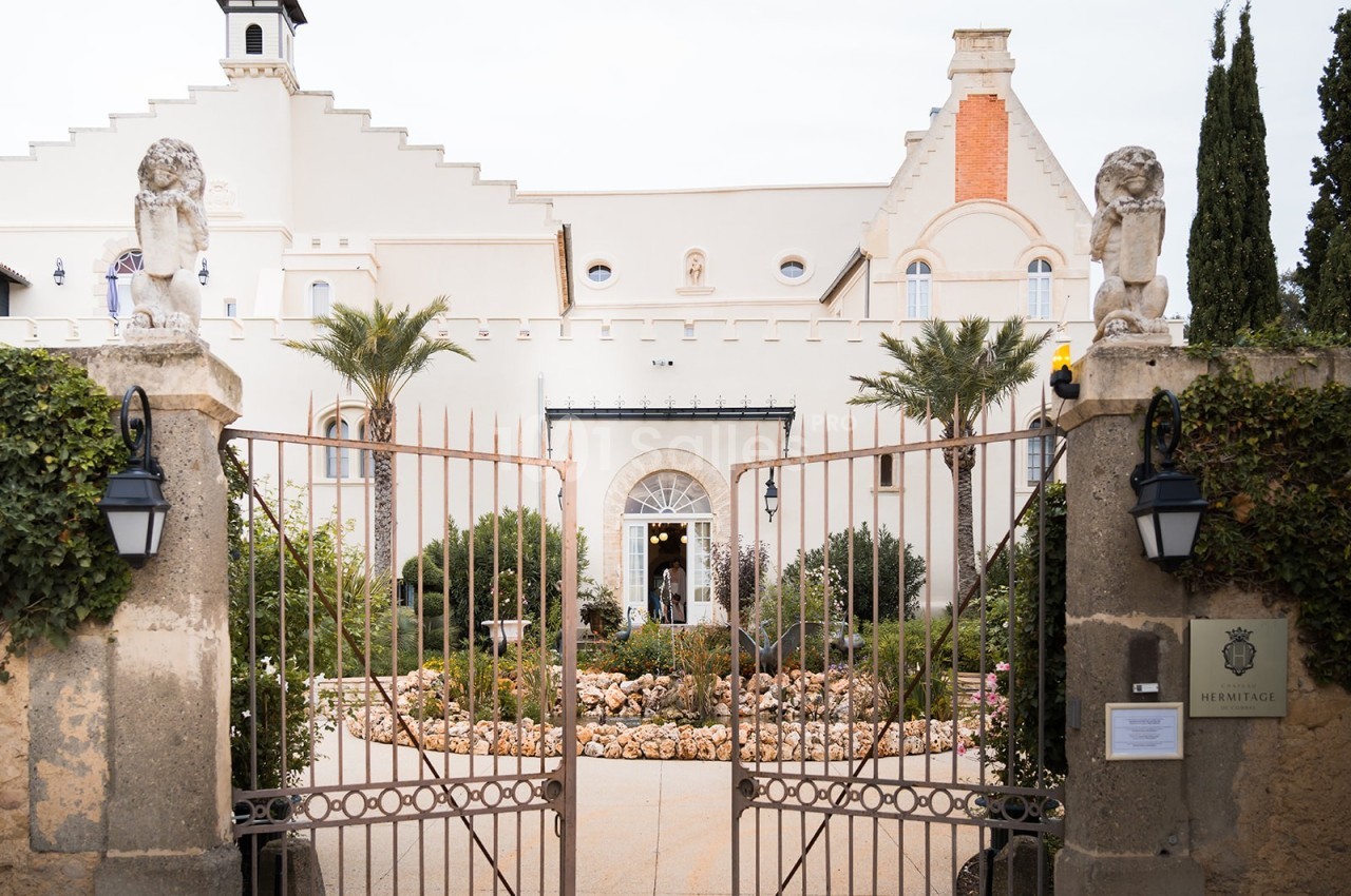 Façade d'un bâtiment historique avec portail en fer forgé, statues de lions et jardin paysager à l'entrée.