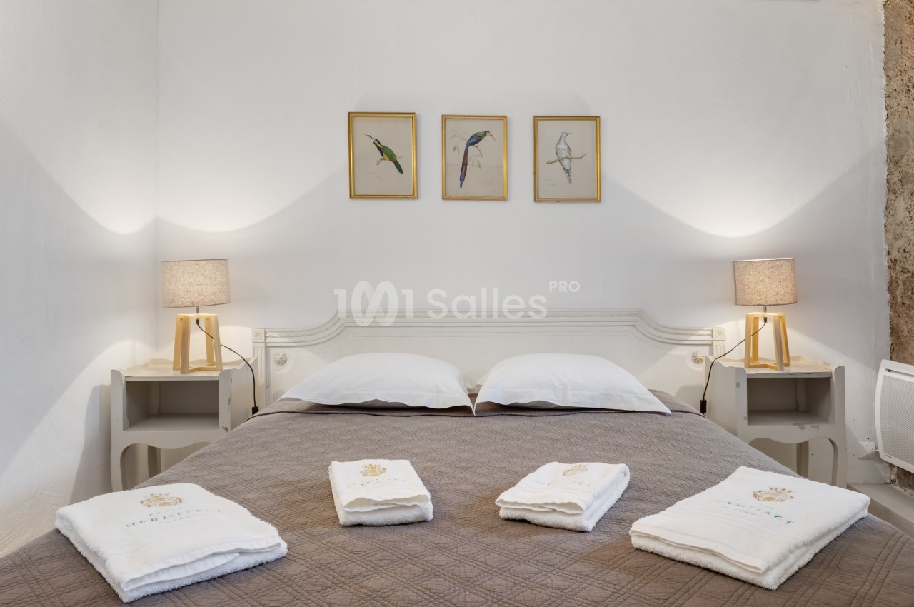 Lit double avec couvre-lit marron, serviettes pliées au premier plan, deux lampes de chevet et trois cadres muraux.