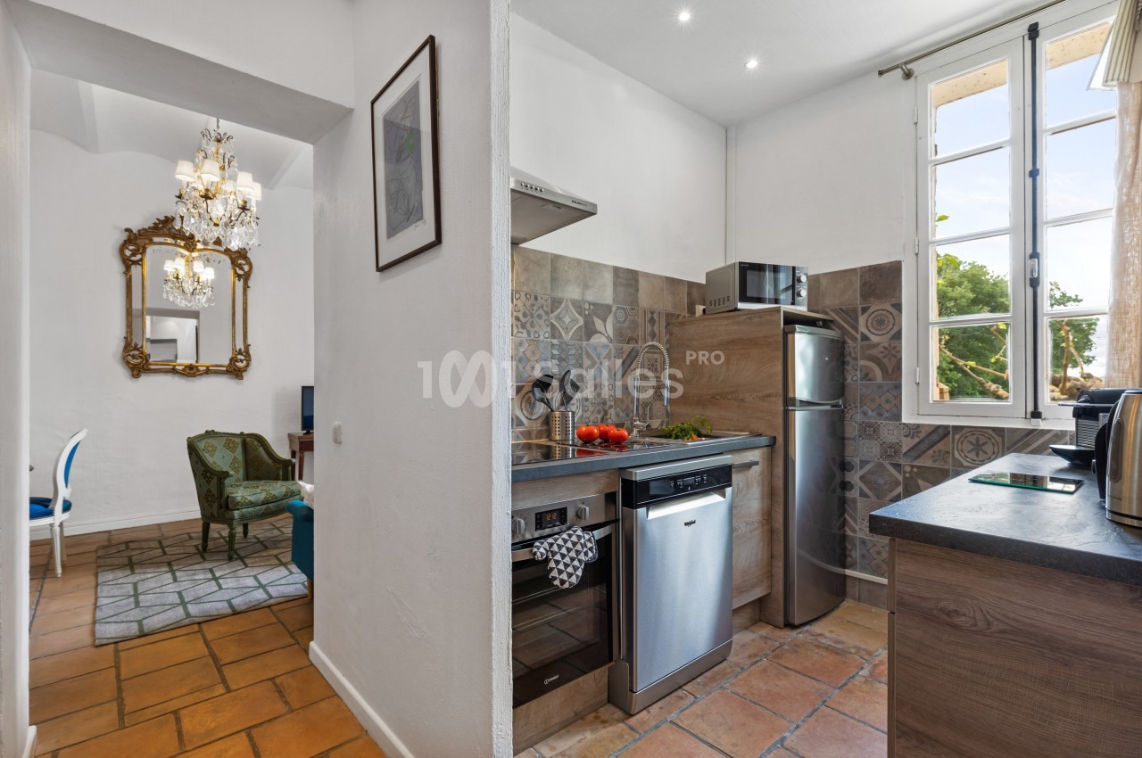 Cuisine lumineuse avec électroménagers modernes, carrelage décoratif, et vue sur un espace de vie et l'extérieur.