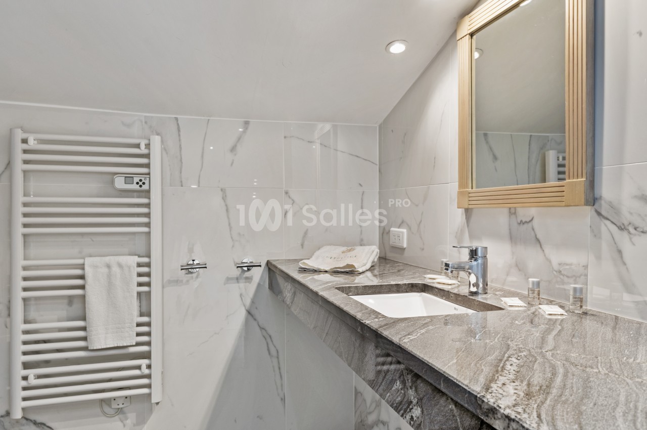 Salle de bain avec lavabo en marbre, miroir encadré, porte-serviettes chauffant et murs en carrelage effet marbre.