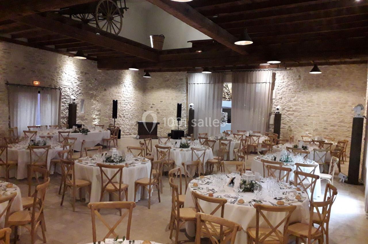 Salle de réception avec des tables rondes dressées, chaises en bois et murs en pierre apparente.
