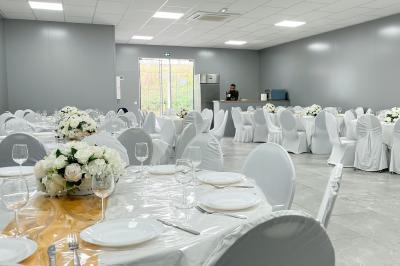 Salle de réception avec tables rondes couvertes de nappes blanches, chaises bleues et une scène avec rideaux bleus.