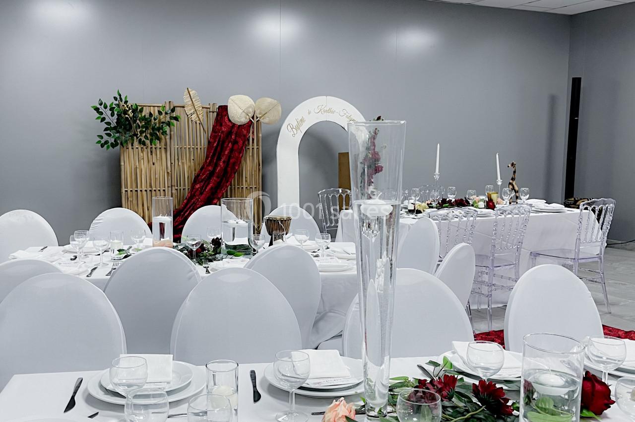 Salle de réception décorée avec des tables dressées, nappes blanches, fleurs rouges et un décor en bambou en arrière-plan.