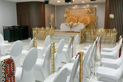 Salle de réception avec tables rondes couvertes de nappes blanches, chaises bleues et une scène avec rideaux bleus.