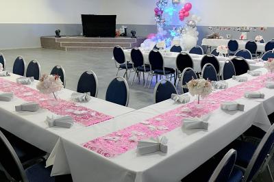 Salle de réception avec tables rondes couvertes de nappes blanches, chaises bleues et une scène avec rideaux bleus.