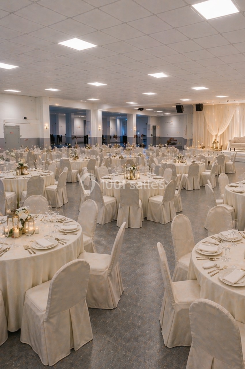 Salle de réception décorée avec des tables rondes dressées, nappes blanches et centre de table lumineux.