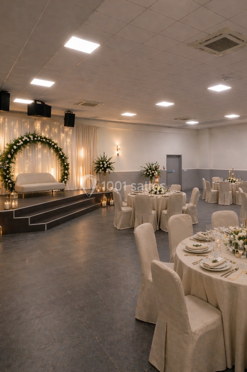 Salle de réception décorée avec des tables rondes dressées, une arche florale lumineuse et un éclairage chaleureux.