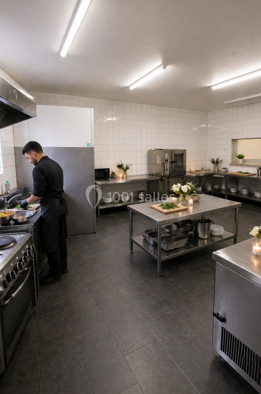 Un chef cuisine dans une grande cuisine professionnelle équipée de plans de travail en acier inoxydable.