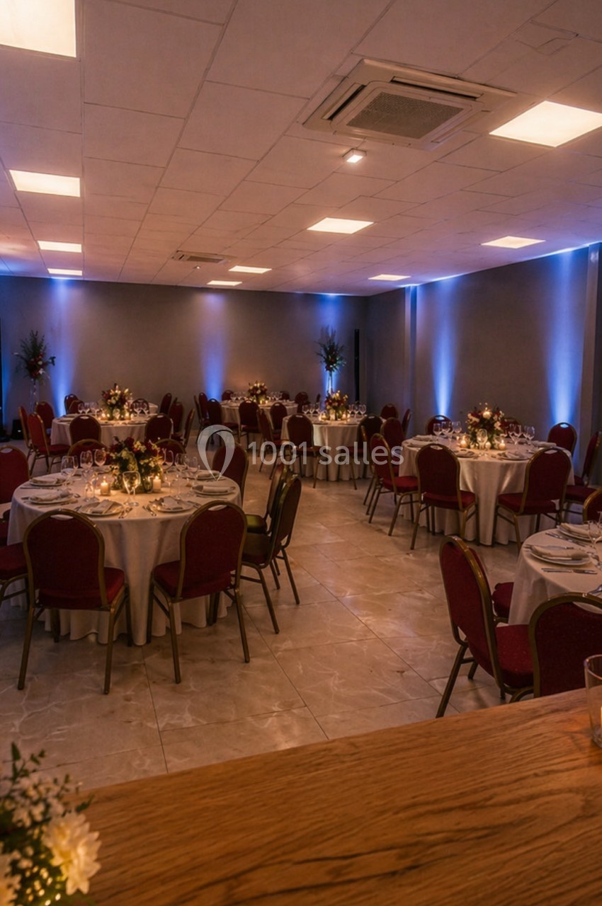 Salle de réception avec tables rondes dressées, éclairage tamisé et décorations lumineuses.