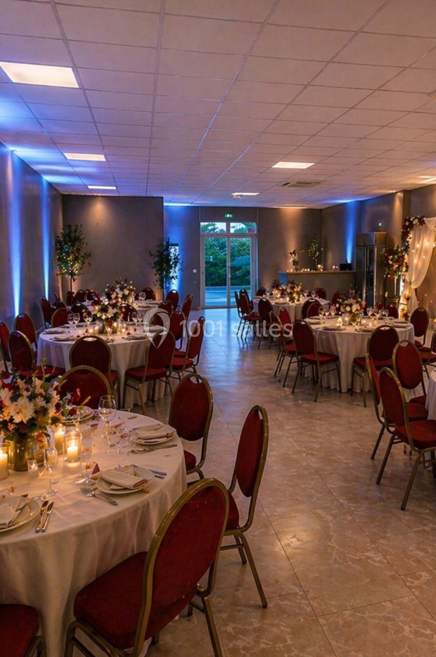 Salle de réception décorée avec des tables rondes dressées, éclairage tamisé et ambiance festive.