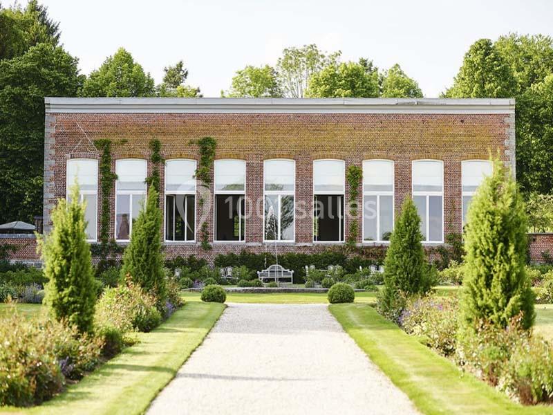 Bâtiment en briques rouges avec de grandes fenêtres, entouré d'un jardin paysager et d'une allée centrale gravillonnée.