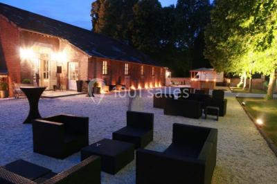 Cour pavée éclairée par des bougies et lumières chaudes, avec un bâtiment historique en arrière-plan, de nuit.