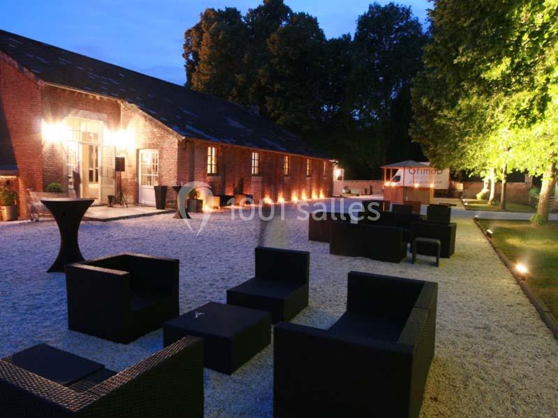 Cour extérieure en soirée avec mobilier de jardin noir, éclairage chaleureux et bâtiment en briques en arrière-plan.