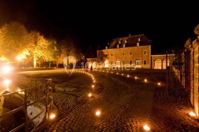 Cour pavée éclairée par des bougies et lumières chaudes, avec un bâtiment historique en arrière-plan, de nuit.