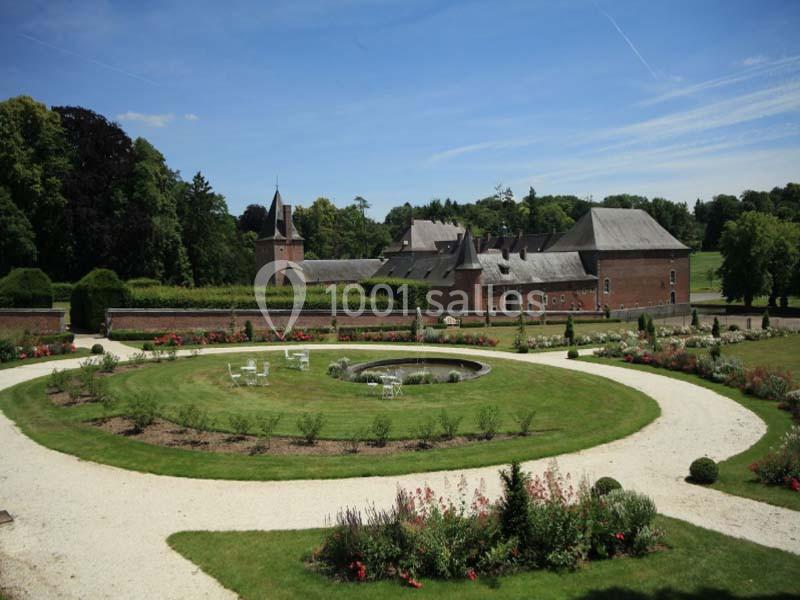 Jardin paysager avec pelouses, parterres fleuris, allées en gravier et un bâtiment en briques entouré de verdure.