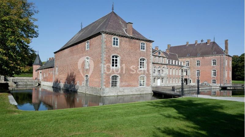 Bâtiment en briques rouges avec douves, entouré de pelouse et d'arbres, sous un ciel dégagé.