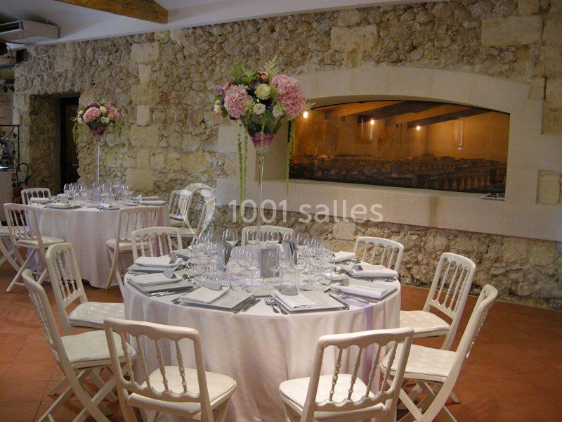 Salle de réception avec tables rondes dressées, nappes blanches, chaises assorties et décoration florale élégante.