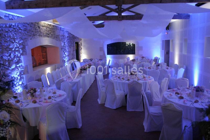 Salle de réception décorée pour un mariage, avec des tables dressées, des chaises couvertes et un éclairage tamisé.