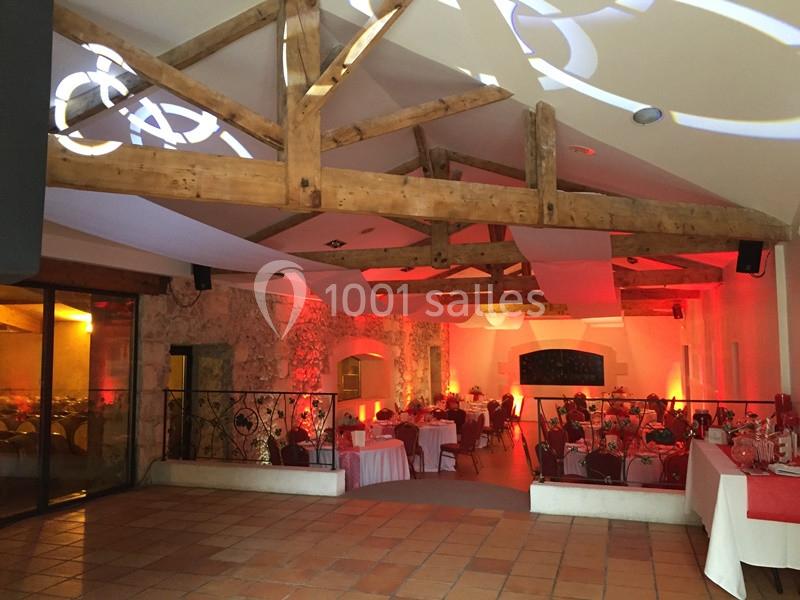 Salle de réception avec poutres apparentes, tables dressées et éclairage chaleureux dans un décor en pierre.
