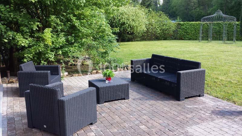 Mobilier de jardin en résine tressée noir disposé sur une terrasse pavée, entourée de verdure.