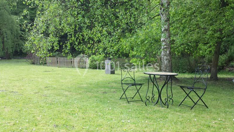 Table et deux chaises en fer forgé sur une pelouse, entourées d'arbres et d'une petite clôture en bois.