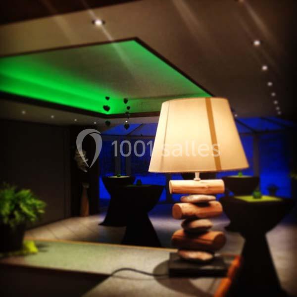 Lampe design en bois au premier plan dans une salle moderne avec éclairage tamisé et ambiance colorée.