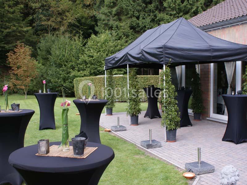 Tentes noires et tables hautes décorées dans un jardin, aménagées pour un événement en extérieur.