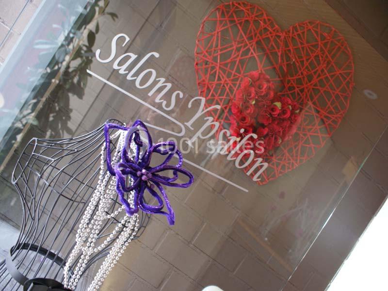 Cœur rouge décoratif et mannequin orné de perles et d'une fleur violette devant une vitrine ’Salons Ypsilon’.