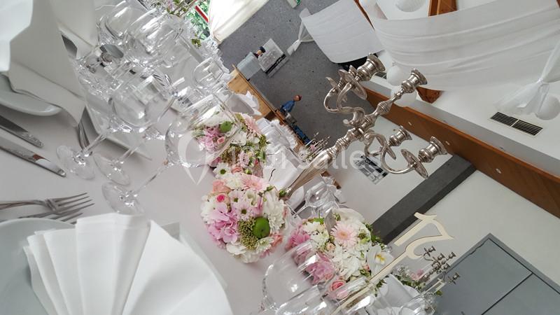 Table de réception élégamment dressée avec nappes blanches, chandeliers argentés et bouquets de fleurs roses et blanches.