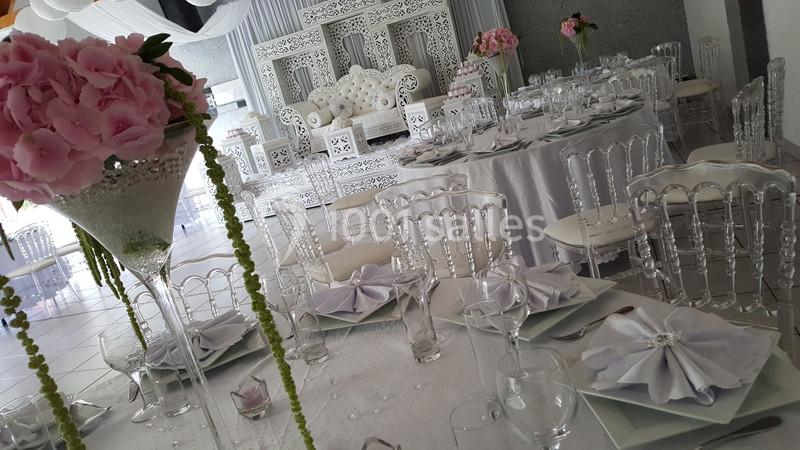 Salle de réception décorée avec des tables élégantes, des chaises transparentes et des fleurs roses, avec un canapé blanc en…