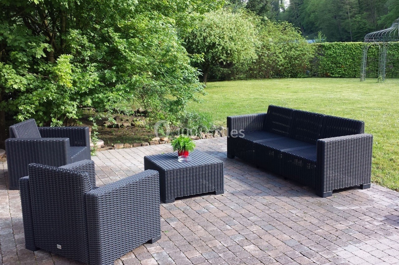 Salon de jardin en résine tressée noire avec table basse, disposé sur une terrasse pavée, entourée de verdure.