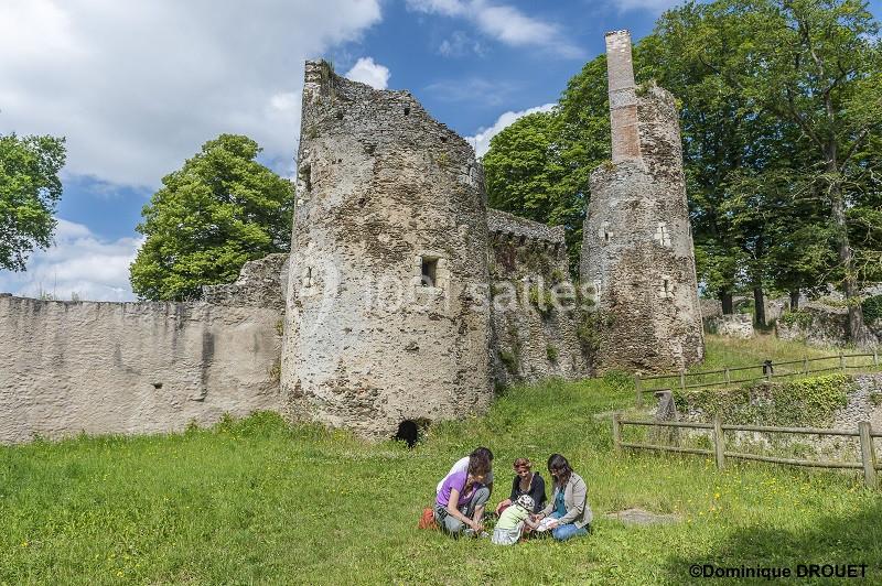 Ruines d'un château médiéval entourées de verdure, avec trois personnes assises sur l'herbe au premier plan.